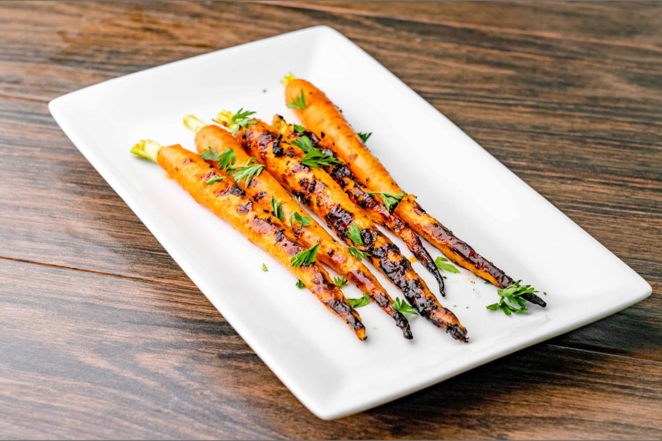 Grilled carrots with herbs on a white plate on a wooden table