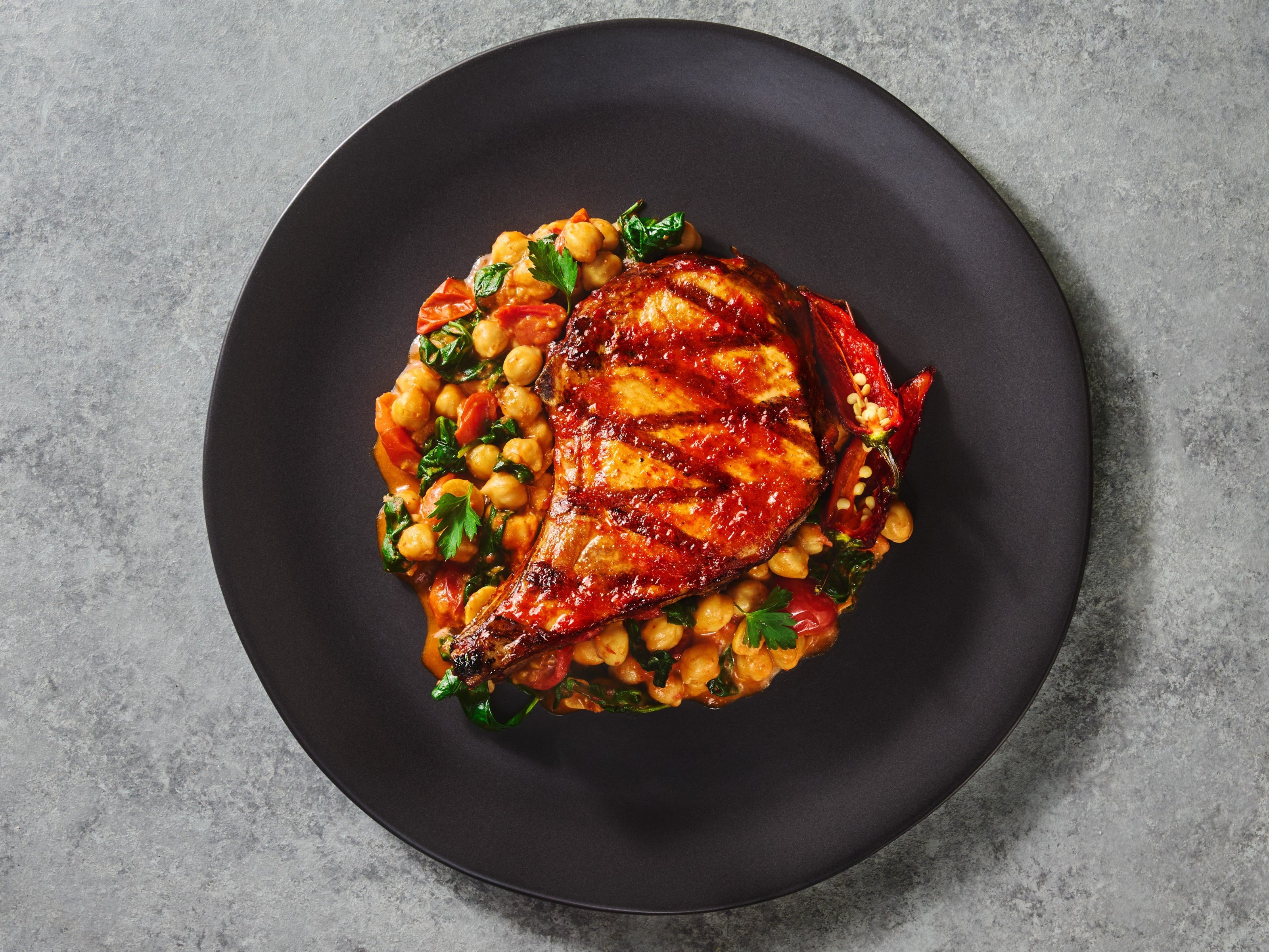 Grilled chicken with chickpea and vegetable salad on a black plate against a gray background